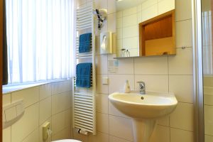 Ein Badezimmer mit Blick zum Fenster mit Spiegel, ein Fön und petrolfarbene Hantücher, die auf dem Badheizkörper hängen
