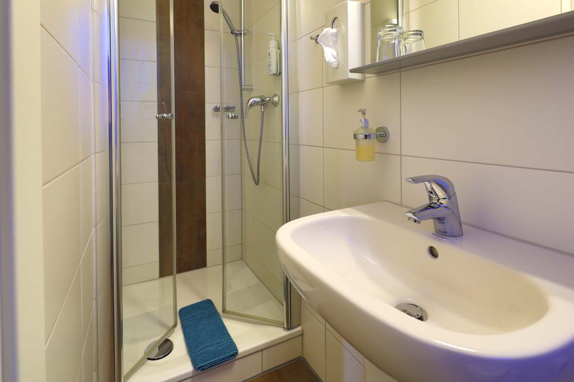 Ein Badezimmer mit Blick auf das Waschbecken mit Spiegel, ein Kosmetikspiegel und Kosmetiktücher sowie Seife ind der Dusche ist vorhanden