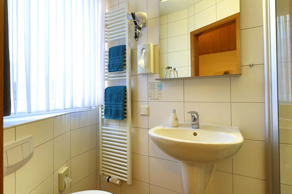 A bathroom with a view of the window with a mirror, a hair dryer and teal towels hanging on the towel radiator