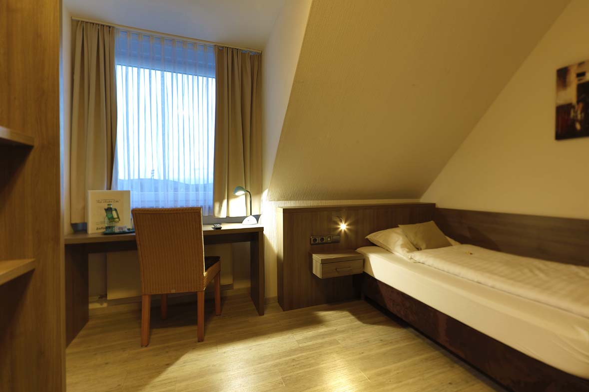 A hotel room with a view of the single bed, the desk is in front of the window with enough light