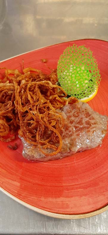 Meat with brown roasted onions on red plate with deco
