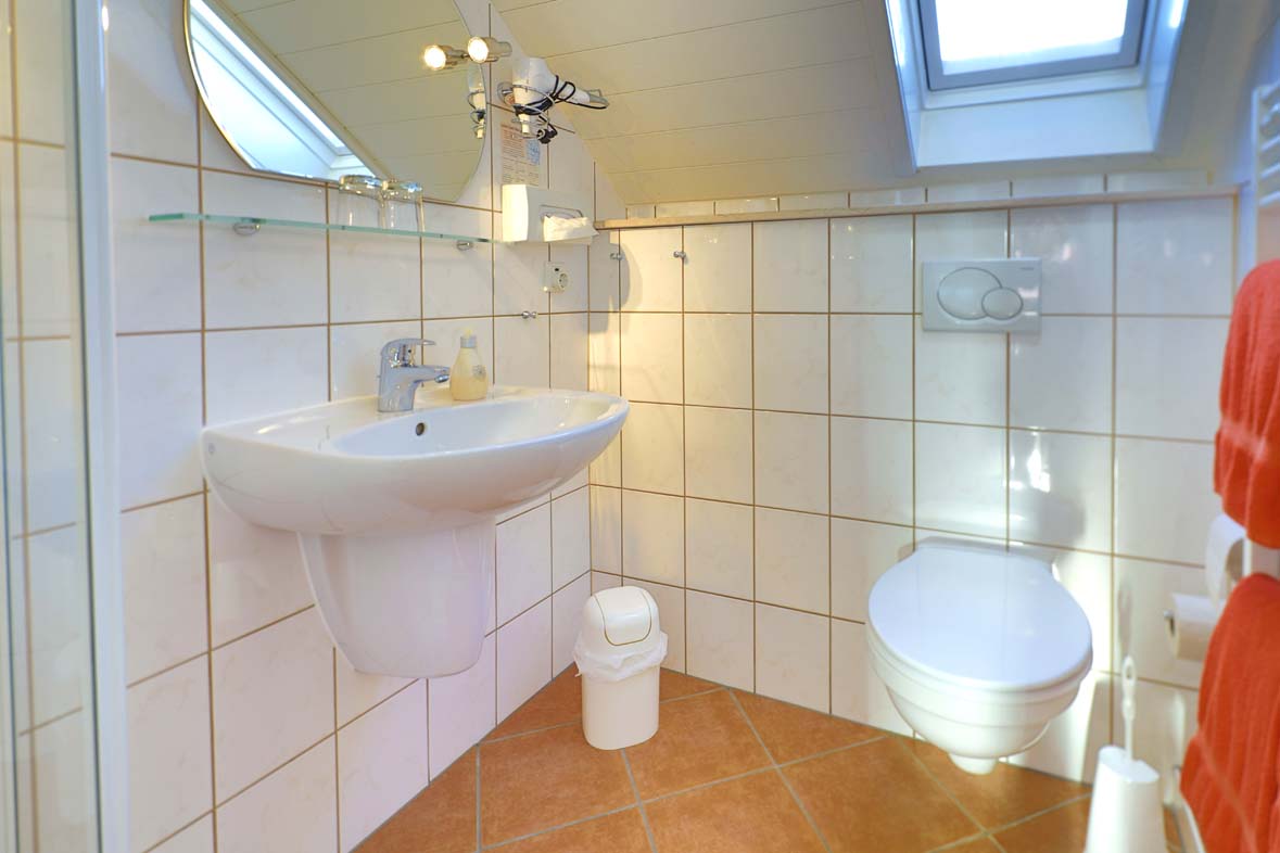 Badezimmer mit Fenster in der Dachschräge weiße Wandfliesen, Fußboden und Hanttücher sind terracottafarben