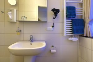 Ein Badezimmer mit Blick auf das Waschbecken mit Spiegel, ein Fön und petrolfarbene Hantücher