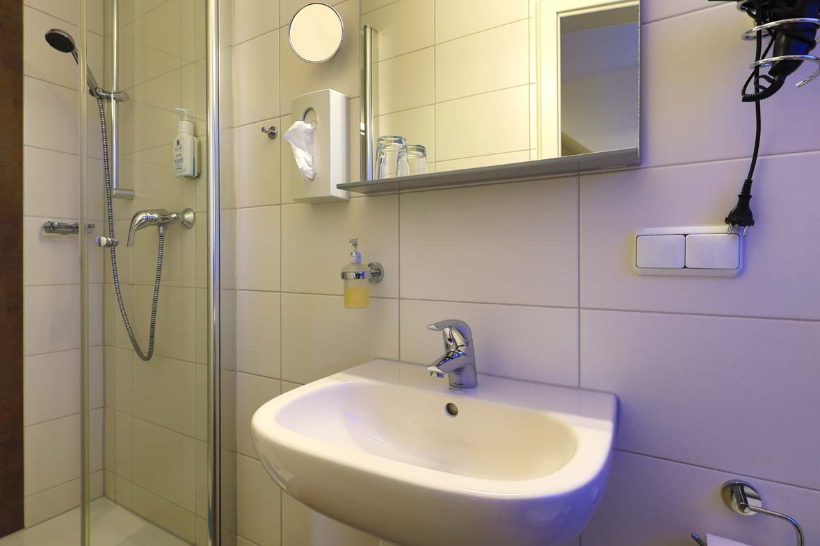 A bathroom with a view of the sink with a mirror, a make-up mirror and facial tissues and soap in the shower is available