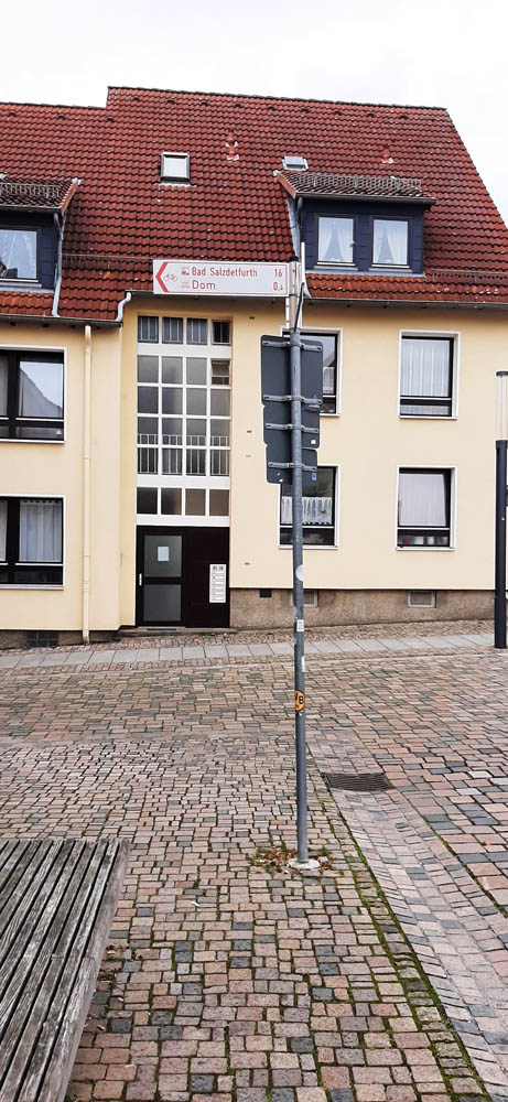 Signpost on cobblestones, in the background a yellow house with a red roof